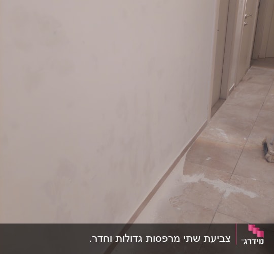 קיר צבוע עם סימני תיקון וציוד צביעה על הרצפה